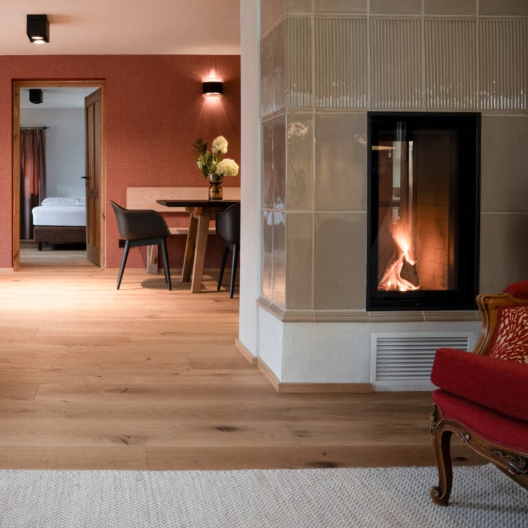 Foto vom Oidn Knoglerhof: Feuer im Karmin brennt, man blickt zum Esstisch und zu dem geöffnetem Schlafzimmer.